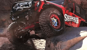 Skyjacker offroad red and black jeep pictured climbing giant red rocks showing lift kit modifications and accessories from Accelerate Auto Repair in Rowlett Tx