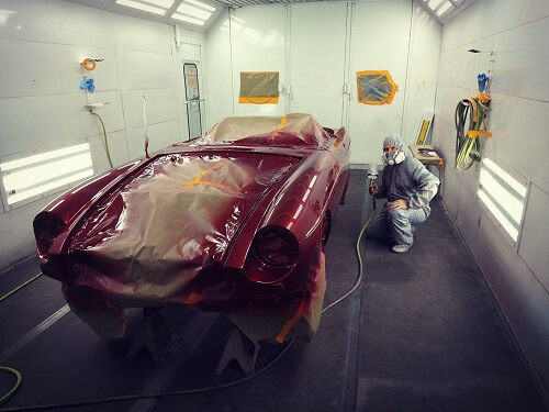 Choosing the Best Paint & Custom Body Work Shop | Accelerate Auto Repair in Rowlett TX. Image of an auto tech spraypainting a red car body.