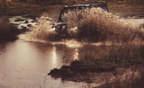 Rock-Crushing Off-Road Modifications You Need Today | Accelerate Auto Repair in Rowlett, TX. Image of SUV splashing water and dirt race on a muddy road.