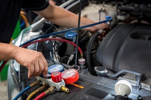 4 Chilling Signs Your Car AC Needs Maintenance & Repair | Accelerate Auto Repair in Rowlett, TX. Closeup image of an auto mechanic checking and fixing a car’s air conditioner system in an auto repair shop.