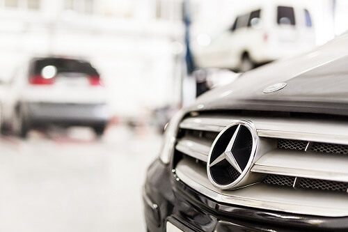 How Auto Repair Of European Vehicles Differ from Asian & Domestic Cars | Accelerate Auto Repair in Rowlett, TX. Closeup image of a Mercedes-Benz car grill at an auto repair station with other European vehicles in the background.