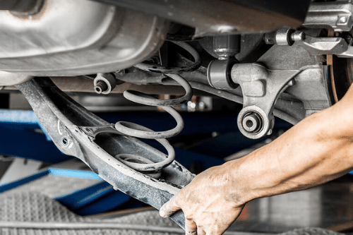 Hand of an Accelerate Auto Repair technician checking the suspension underneath a vehicle