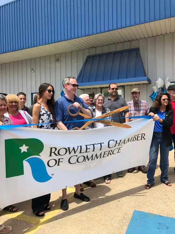 Owner of Accelerate Auto Repair Justin Cole, cuts red ribbon with giant scissors for the Rowlett Tx Chamber of Commerce Grand Opening, with a crowd of loved ones gathered behind him, learn more about Accelerate Auto Repair
