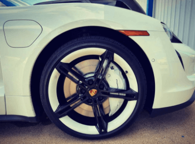 Image of pearl white porsche brake pads peaking through black rims on passenger tire that came in for auto repair at Accelerate Auto Repair in Rowlett Tx