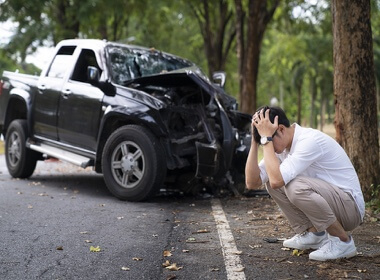 Accelerate Auto Repair in Rowlett Tx; image of young caucasian man squatting with his hands on his head near a tree that his 4 door black pickup truck just ran into