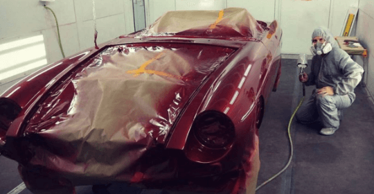 one of the body shop mechanics in protective gear is painting an old performance vehicle a candy apple red in the paint bay at Accelerate Auto Repair in Rowlett Tx