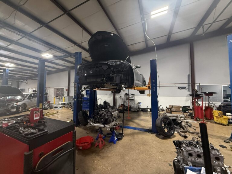 A vehicle on a lift with its removed engine and subframe assembly on stands below it inside the Accelerate Auto Repair shop.