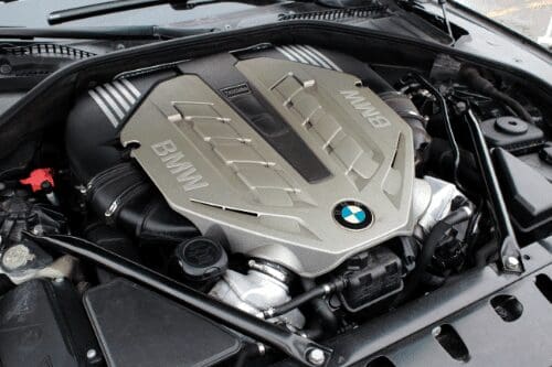 A vehicle engine bay with the engine cover in view, the general area where an AC compressor is mounted and driven by a belt.