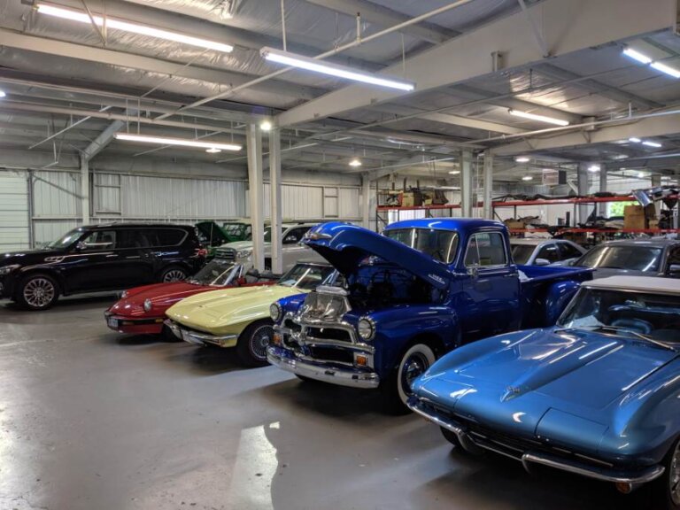 Cars parked inside a repair shop, including a blue classic pickup with its hood open.