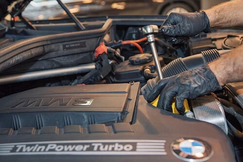 Technician working on a BMW engine with the TwinPower Turbo cover in view.