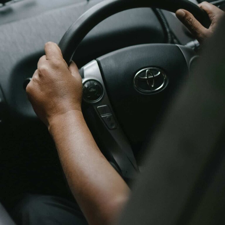 A driver holding the steering wheel of a Toyota with both hands.