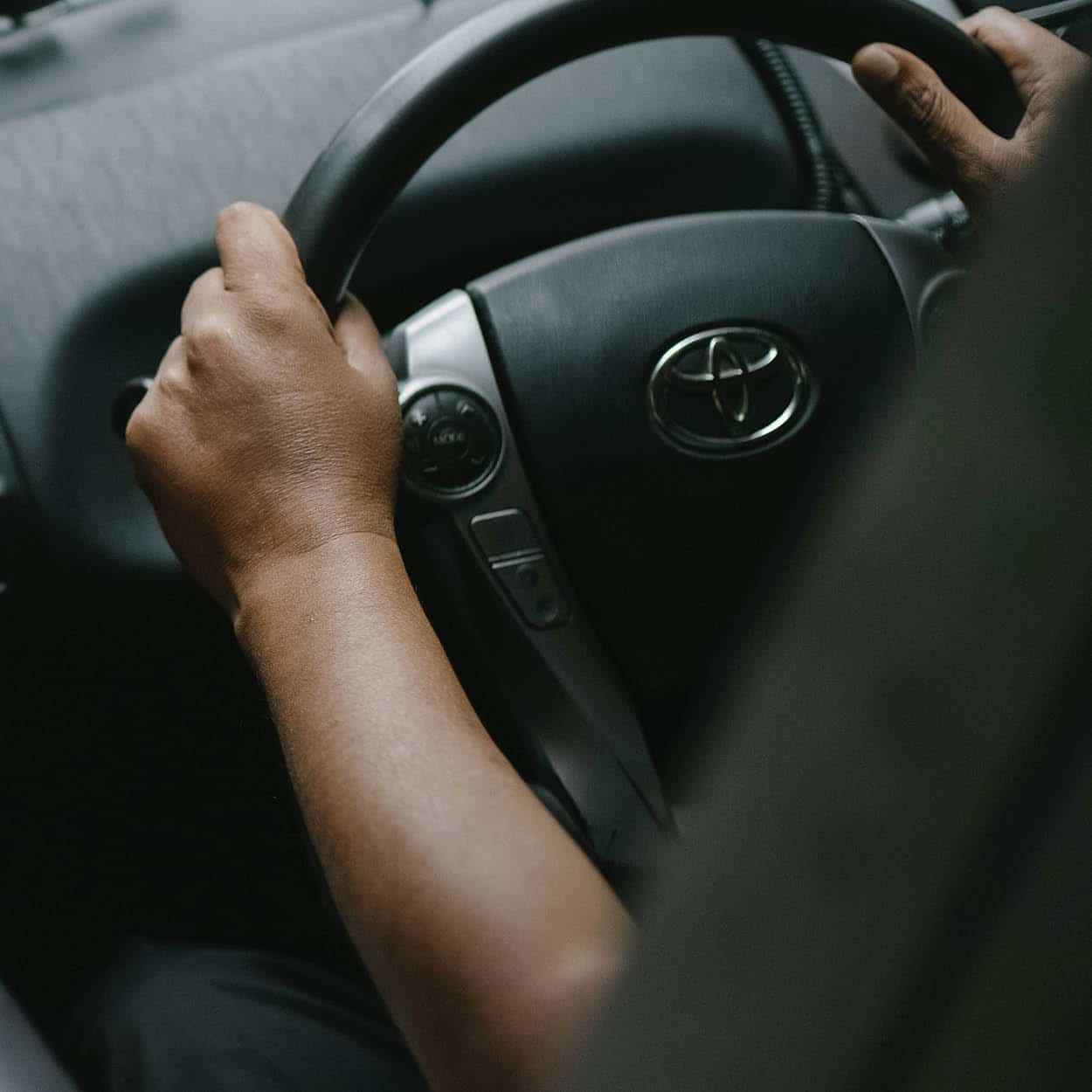 A driver holding the steering wheel of a Toyota with both hands.