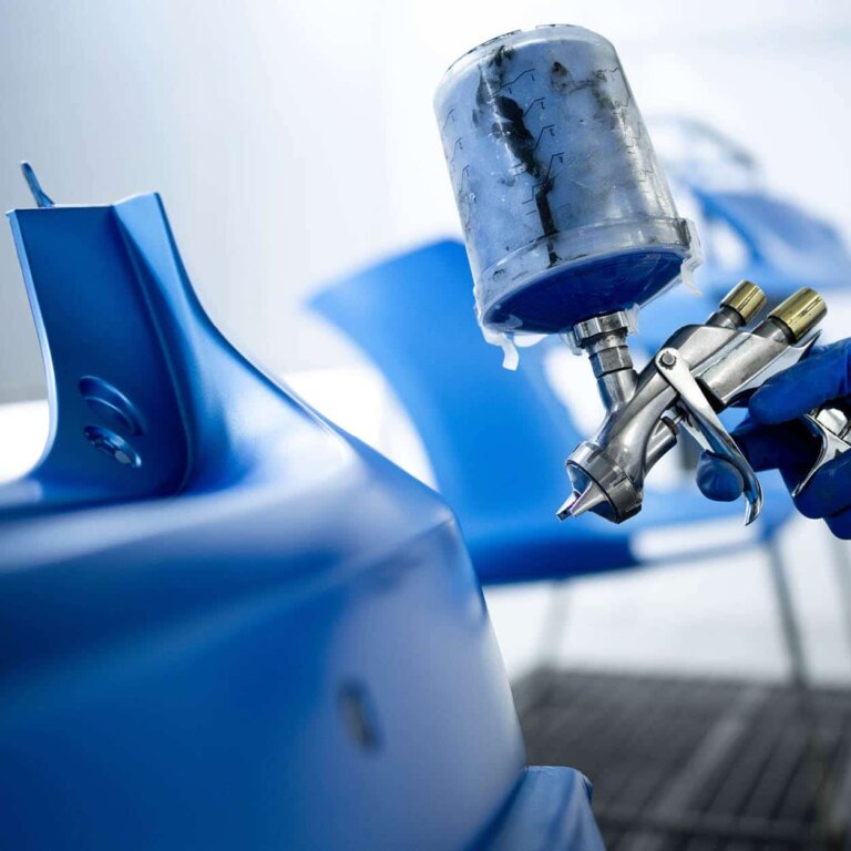 A vehicle bumper being painted with a spray gun.
