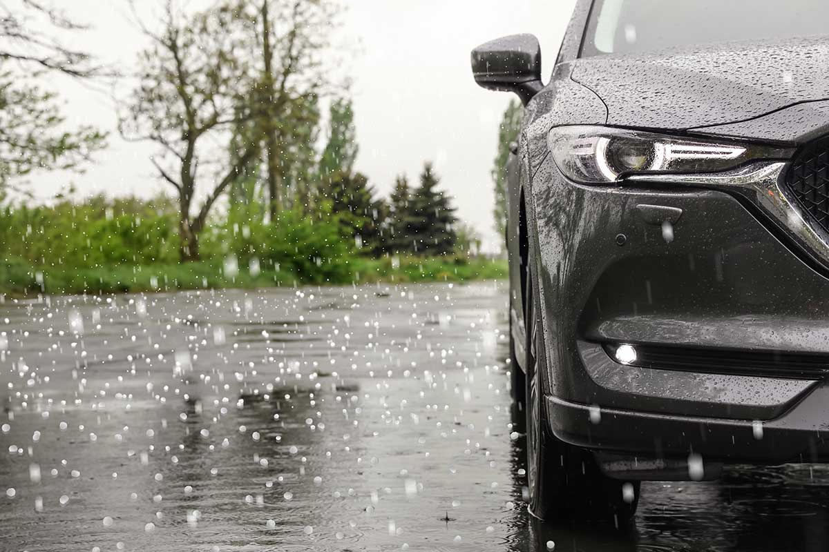 Hailstones falling on wet pavement beside the front of a dark gray SUV.
