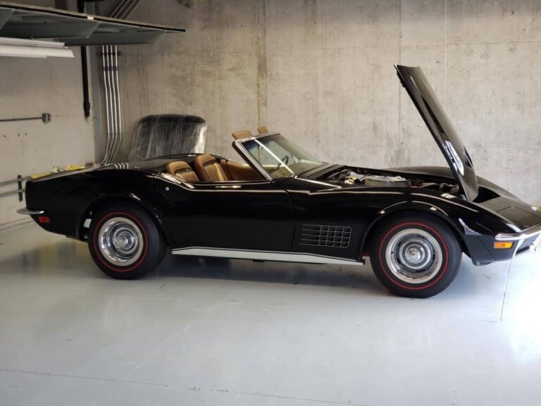 A black classic Corvette convertible with its hood open in a garage.