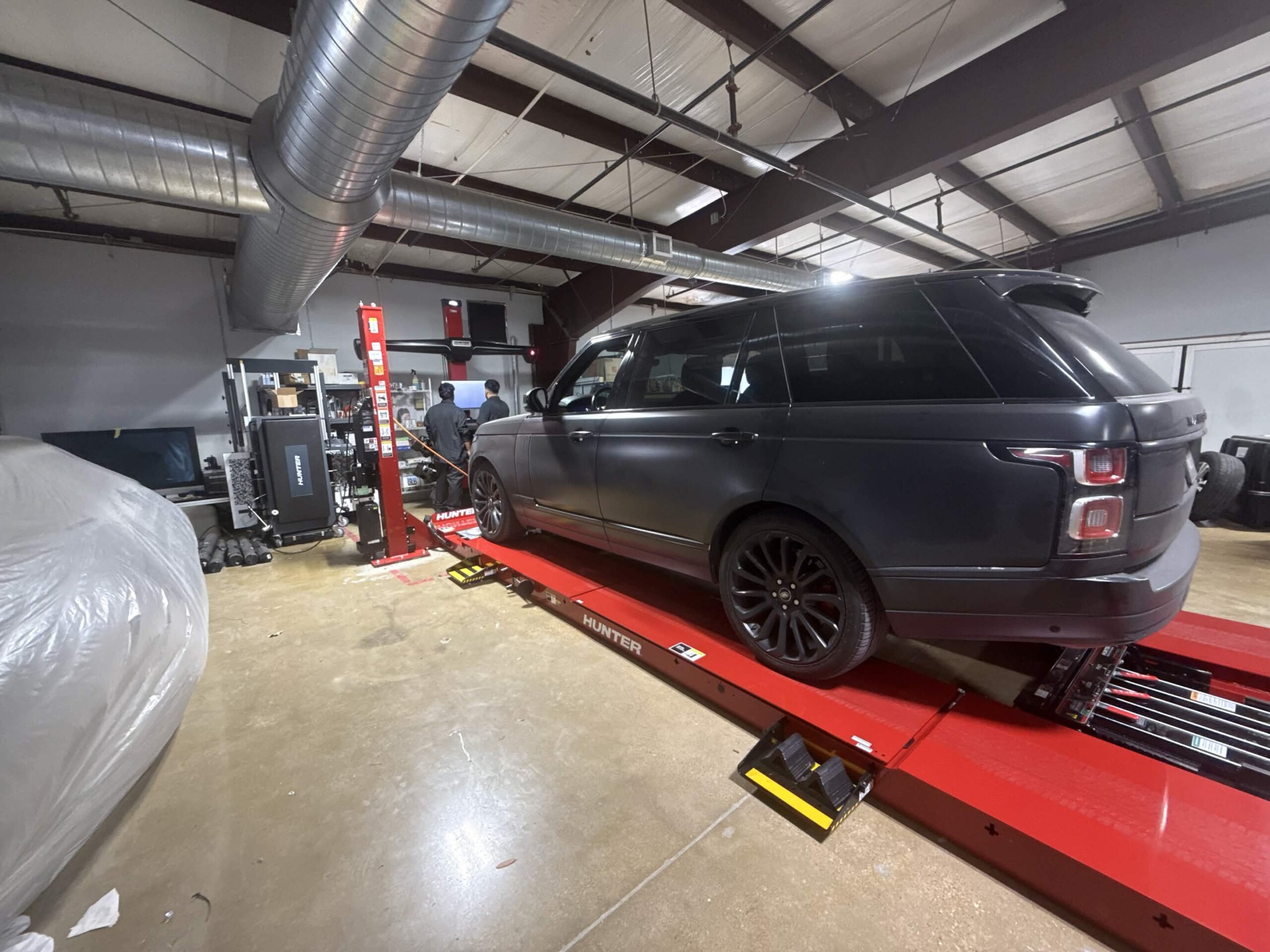 Dark gray Range Rover on a red Hunter alignment rack inside the shop, with two people at the alignment console.
