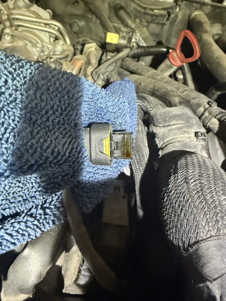 A Mercedes wiring connector removed during teardown at Accelerate Auto Repair, with oil contamination visible inside the connector body.
