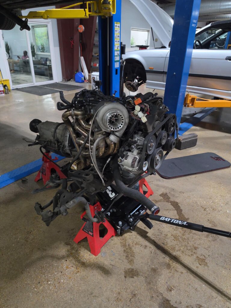 A turbocharged engine and transmission assembly on stands inside the Accelerate Auto Repair shop.