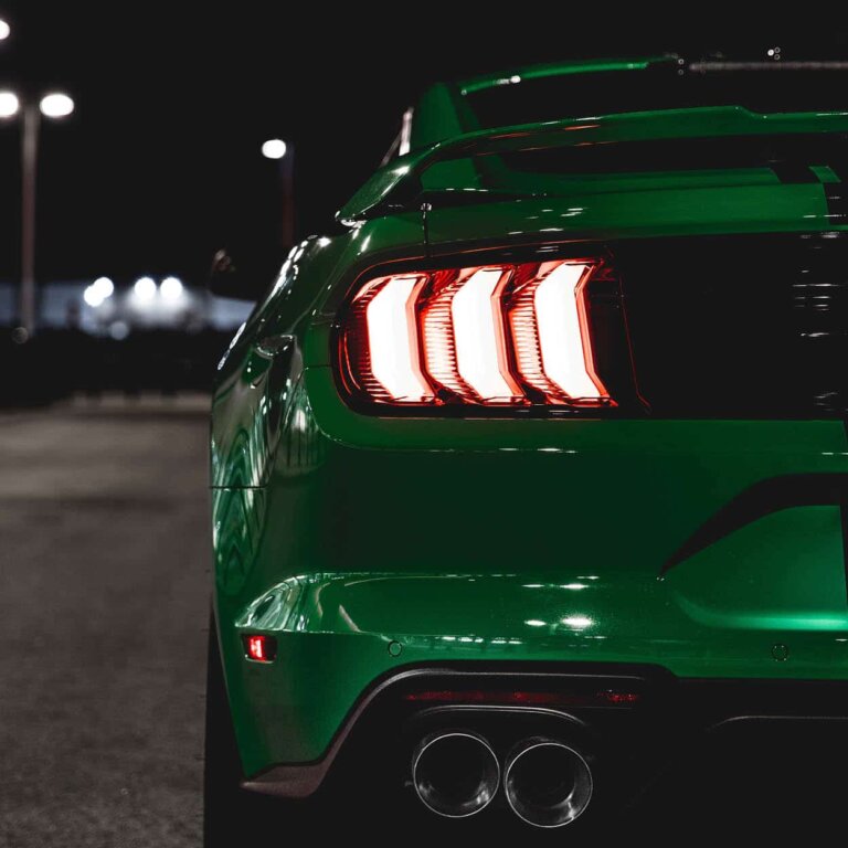 The rear of a green Ford Mustang at night, showing its dual exhaust tips.