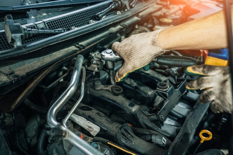 A technician in work gloves using a wrench in a car engine bay.