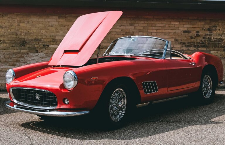 A red classic convertible sports car with its hood open, parked outside.