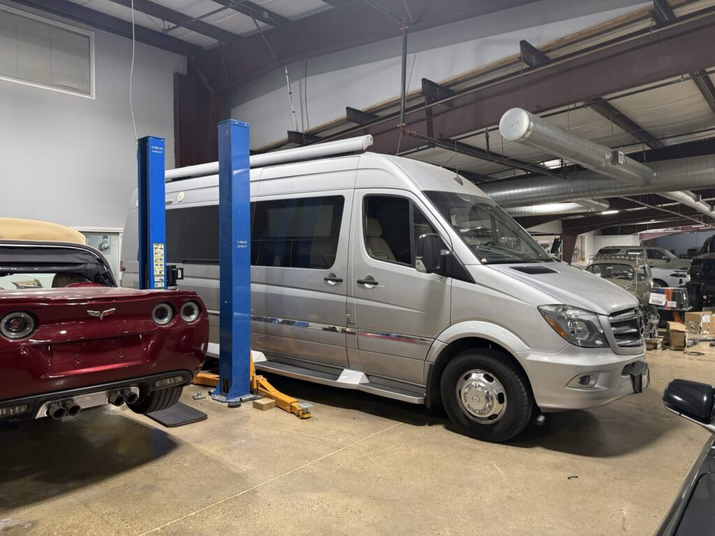 A Mercedes Sprinter van raised between the lift posts in the service bay at Accelerate Auto Repair in Rowlett, Texas.