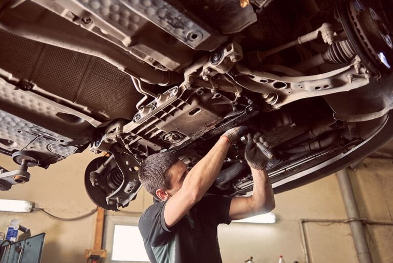 A technician working on the underside of a car raised on a lift.