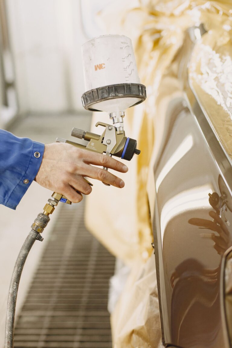 Technician spray painting a car panel with a paint gun