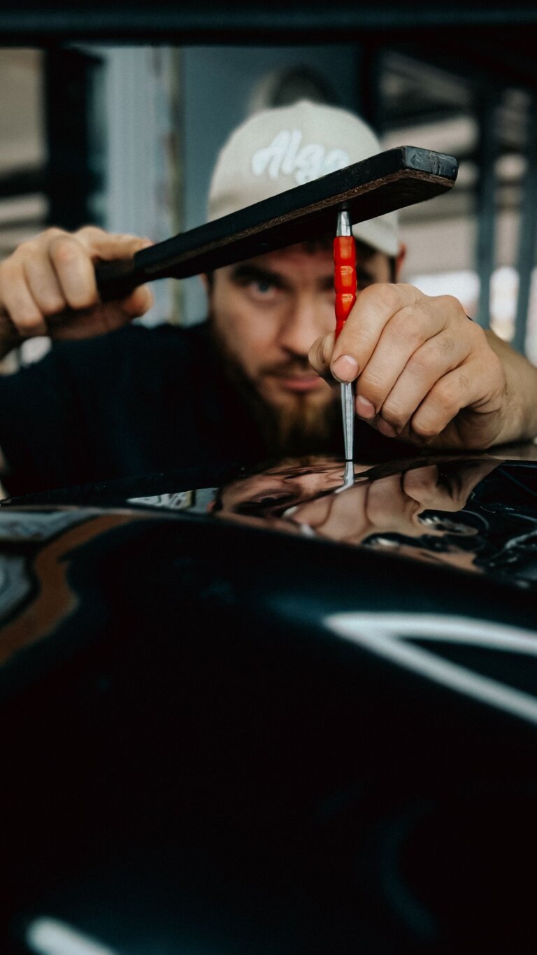 Technician using a tool to work out a dent in a car panel
