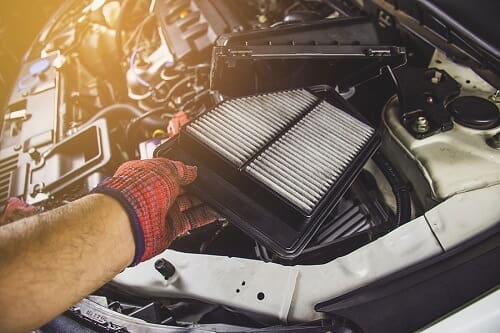 An air filter held near a vehicle engine bay.