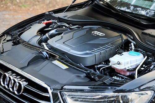 An Audi engine bay with the hood open and the engine cover visible.
