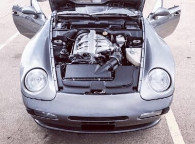 A silver Porsche with its hood open and engine bay visible.
